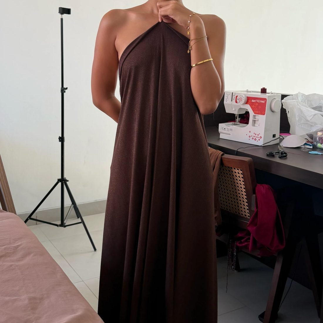 Before: Fera holding a length of brown fabric against her body in the sewing room